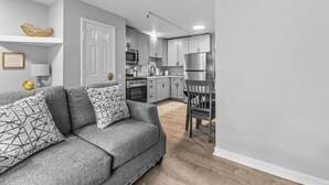 A modern kitchen with grey cabinets, a stainless steel refrigerator, and a dining area with a wooden table and chairs. - Cozy 1BR in Winooski! (Winooski)