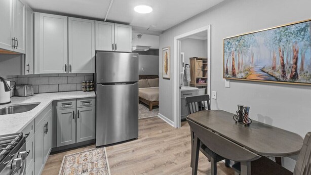 A modern kitchen with grey cabinets, a stainless steel refrigerator, and a dining area with a table and chairs. - Cozy 1BR in Winooski! (Winooski)