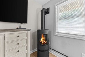 Une chambre moderne avec un poêle à bois noir, une commode blanche et une grande fenêtre équipée de stores.