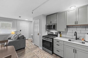 Une cuisine compacte avec des meubles gris, un four à micro-ondes encastré, une cuisinière et un évier.