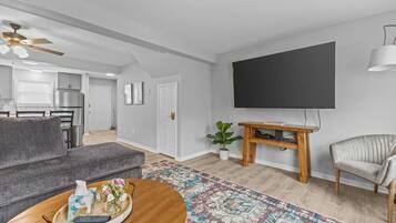 A modern living room with a grey sofa, a wooden coffee table, a flat-screen TV, and a ceiling fan.