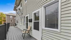 A wooden deck with a chair and a table, a white door with a window, and a mailbox on the side of a house. - Comfortable 2BR in Winooski! (Winooski)