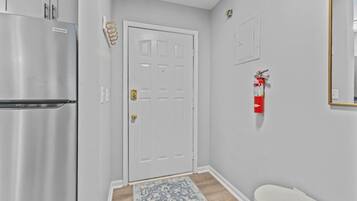 A hallway with a white door, a stainless steel refrigerator, a red fire extinguisher, and a patterned rug.