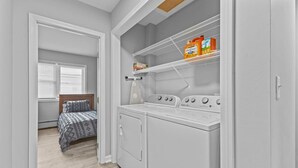 A laundry room with a washing machine, dryer, and shelves with cleaning supplies. - Comfortable 2BR in Winooski! (Winooski)