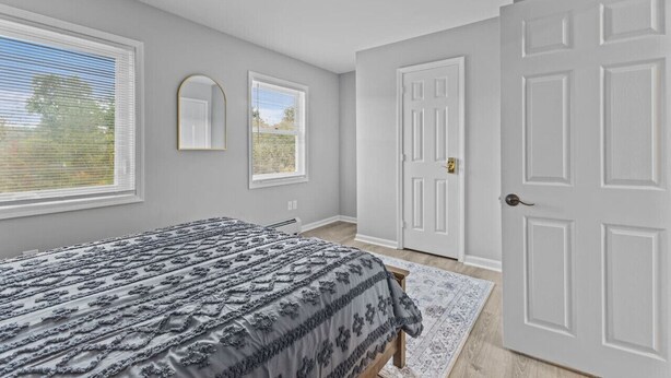 A bedroom with a bed, two windows, a door, and a rug. - Comfortable 2BR in Winooski! (Winooski)