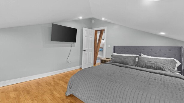 A bedroom with a bed, a flat-screen TV mounted on the wall, and a wooden floor. - Unique Top-Floor Apt in BTV (Burlington)