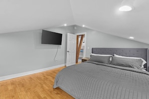 A bedroom with a bed, a flat-screen TV mounted on the wall, and a wooden floor.