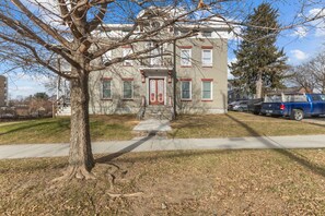 A two-story building with a red door and windows, a tree in the foreground, and a blue pickup truck parked in the background. - Unique Top-Floor Apt in BTV (Burlington)
