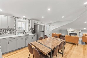 Eine moderne Küche mit grauen Schränken, einem Edelstahl-Kühlschrank und einem Essbereich mit Holztisch und braunen Stühlen.