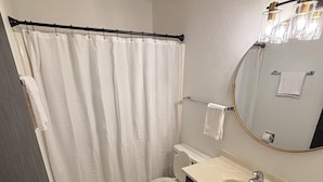 Et badeværelse med toilet, vask, spejl og bruseforhæng.
