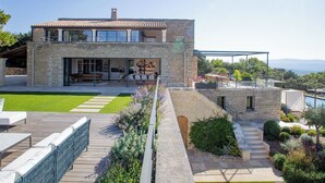 Une maison moderne à deux étages, dotée d’une façade en pierre, d’un grand patio et offrant une vue sur le paysage.