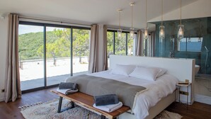 Une chambre à coucher moderne, dotée d’un grand lit, d’un banc et offrant une vue sur un paysage montagneux grâce à de grandes fenêtres.