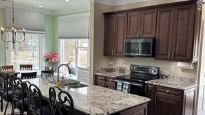 A spacious kitchen with dark wood cabinets, a granite countertop, and a central island with bar stools. - Family-Friendly Lakefront Home with Hot Tub, Firepit, Dock & Breathtaking Views! (Charlotte)