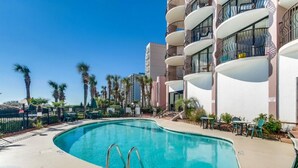 A swimming pool with a curved edge, surrounded by a fence, and adjacent to a multi-story building with balconies. - 3 BR Palms Resort: Oceanfront (Myrtle Beach)