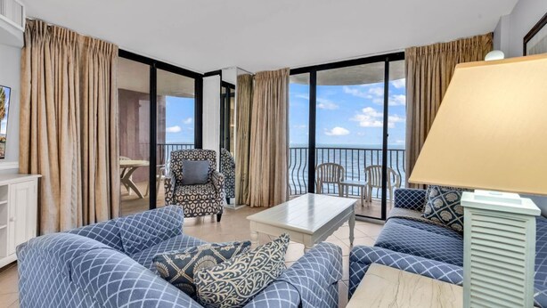 A spacious living room with a sofa set, a coffee table, and a chair. There is a balcony with a view of the sea. - 3 BR Palms Resort: Oceanfront (Myrtle Beach)