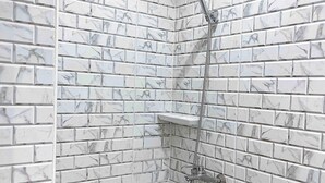 A shower with a marble-patterned wall and a handheld showerhead.