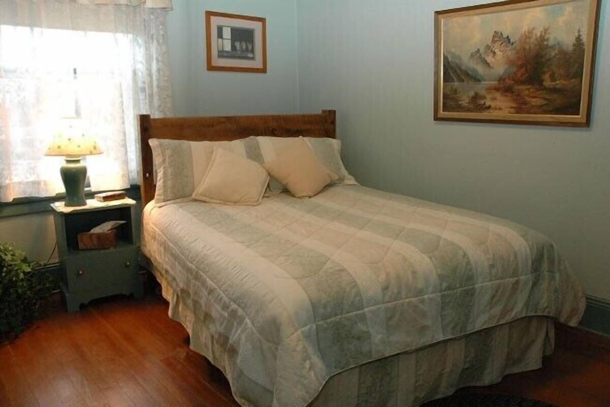A neatly made bed with a wooden headboard, a bedside table with a lamp, and a framed picture on the wall.