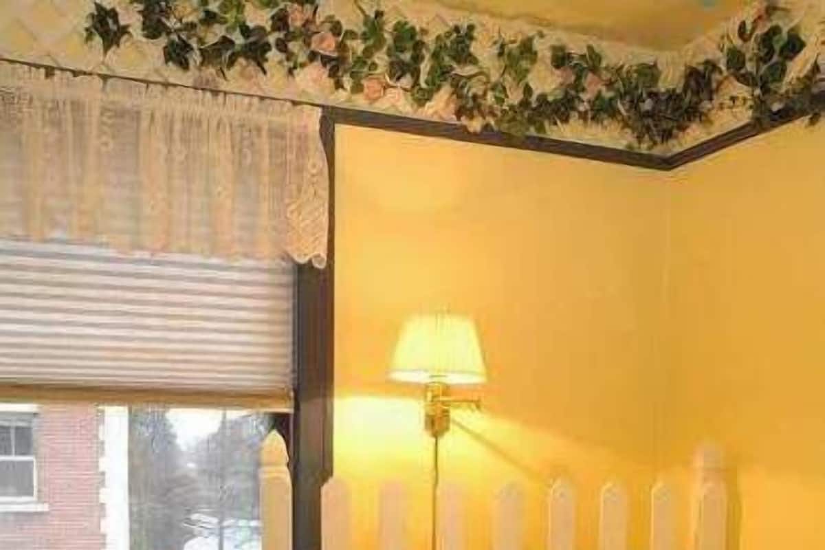 A bedroom with a floral bedspread, a bedside table with a lamp, and a window with blinds.
