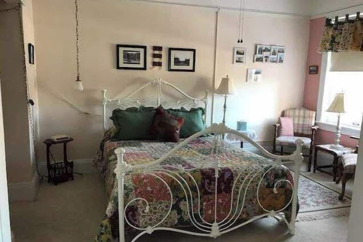 A bedroom with a four-poster bed, a small bedside table, a chair, and a lamp.