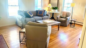 A living room with a sofa, armchair, coffee table, and a small side table with a lamp. - 4 Bedroom Beachside Surfer's Home (South Portland)
