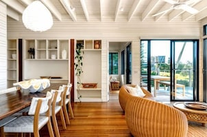 Un interior moderno con comedor, muebles de mimbre y vistas amplias a través de puertas de vidrio.