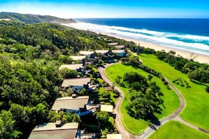 Vista aérea de un complejo turístico costero con casas, un campo de golf y una playa.