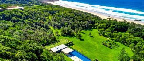 Vista aérea de una propiedad con piscina, exuberante vegetación y una playa.