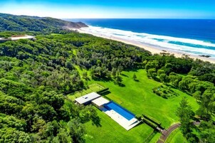 Vista aérea de una propiedad con piscina, exuberante vegetación y una playa.
