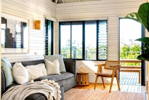 Una habitación con un sofá, una silla, una mesita y un ventanal grande con contraventanas.