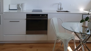 A modern kitchen with white cabinetry, a built-in oven, a coffee maker, and a glass table with a chair. - 1 BR unit with leafy outlook & dedicated workspace (Glebe)