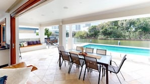 A modern outdoor dining area with a pool view, a seating area with a sofa, and a kitchen area. - Luxico Lakeland Keys (Heated Pool) (Broadbeach Waters)