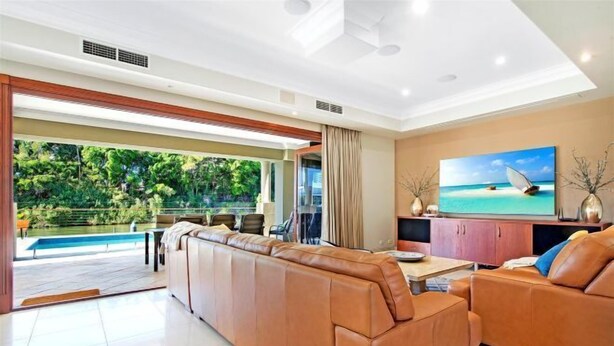 A spacious living room with a large leather sofa, a dining area, and a view of a swimming pool and greenery. - Luxico Lakeland Keys (Heated Pool) (Broadbeach Waters)