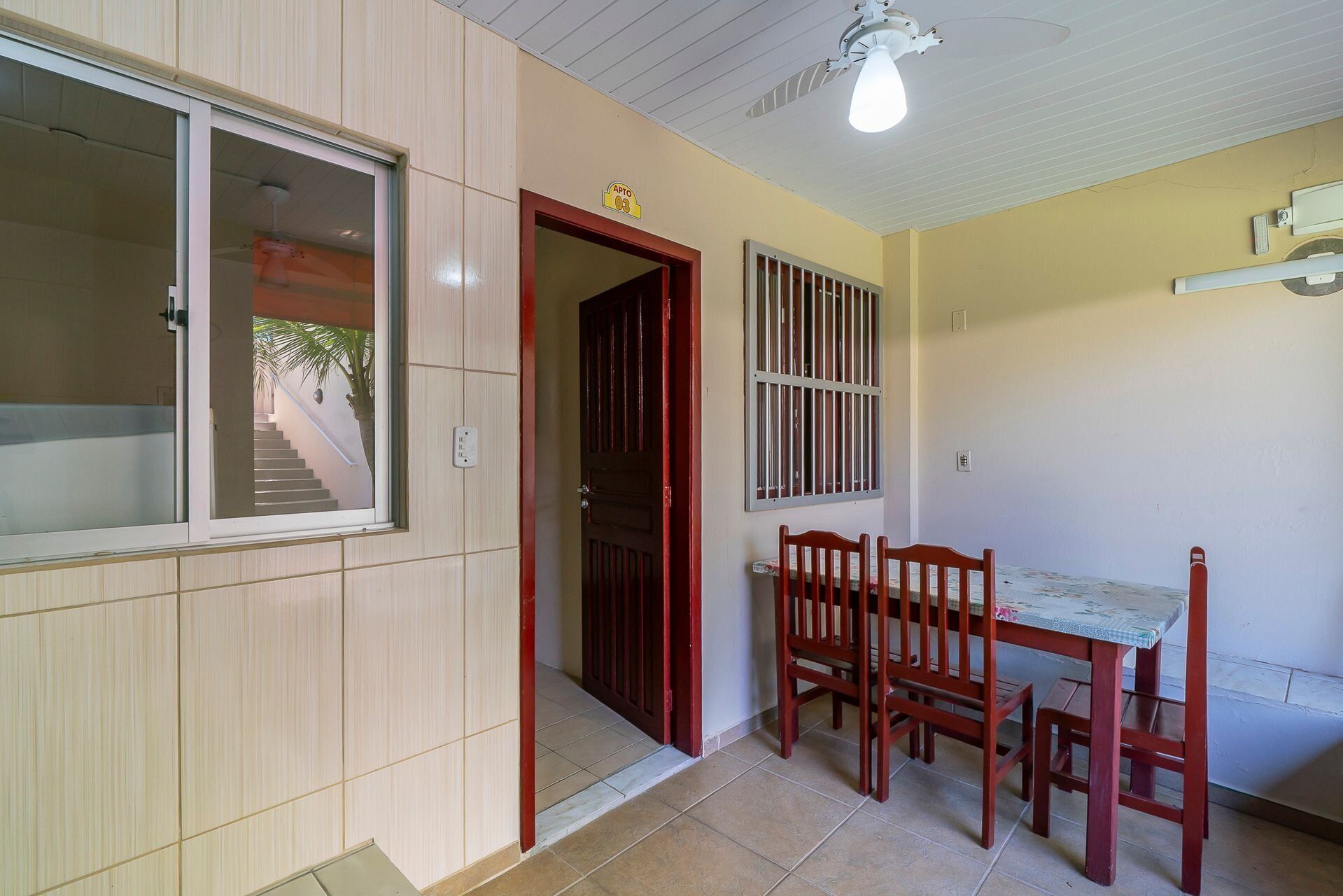 A room with a wooden door, a window with bars, a ceiling fan, and a table with chairs.