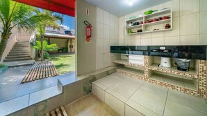 A kitchen with a tiled backsplash, a countertop, and shelves above. - AP 03A - Residencial Solavir (Bombinhas)