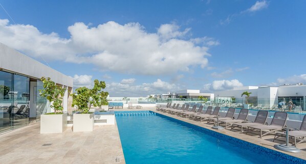A rooftop pool with lounge chairs, potted plants, and modern architecture. - Luxe Apartments near famous 5th Ave (Playa del Carmen)