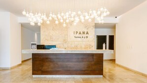 Mostrador de recepción de hotel con pared de mármol, base de panel de madera y una lámpara colgante.