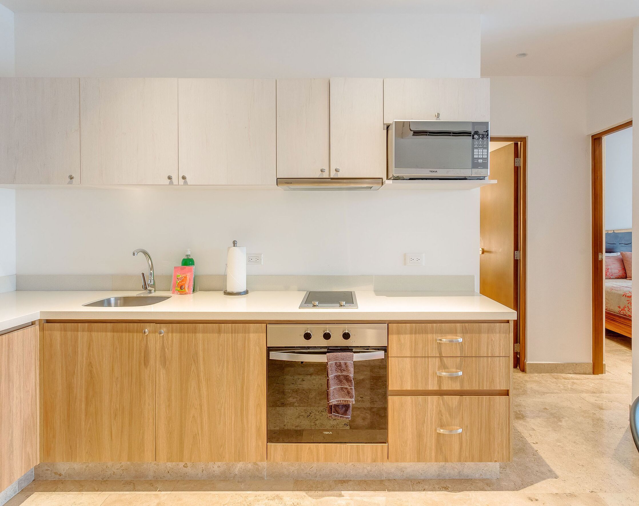 A modern kitchen with wooden cabinets, a stainless steel sink, a built-in oven, and a microwave.