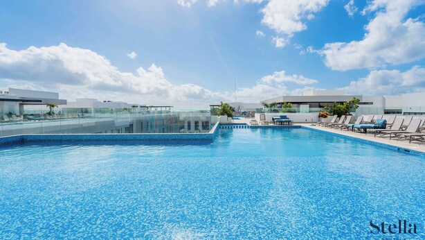 Una piscina con agua azul cristalina, rodeada de sillas de descanso y una barandilla de vidrio.