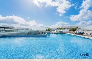 A swimming pool with clear blue water, surrounded by lounge chairs and a glass balustrade. - Luxe Apartments near famous 5th Ave (Playa del Carmen)