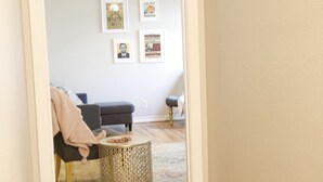 En gang der fører til en stue med en sofa, et rundt sofabord og billeder i rammer på væggen.