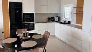 A modern kitchen with white cabinetry, a black dining table with beige placemats, and a built-in oven. - Casa Margarita, Costa Adeje (Costa Adeje)