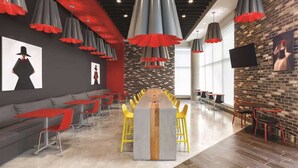 A modern dining area with a long communal table, red and grey pendant lights, and a brick wall with artwork. - Kompose Boutique Hotel Miami Airport  (Miami)