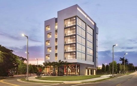 A modern multi-story hotel with a prominent glass facade, multiple balconies, and a well-lit entrance area.