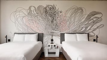 Habitación de hotel con dos camas, un cuadro abstracto grande en la pared, una mesita de noche con lámpara y piso de madera.