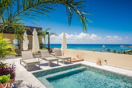 A poolside area with lounge chairs and umbrellas, overlooking a beach and ocean.