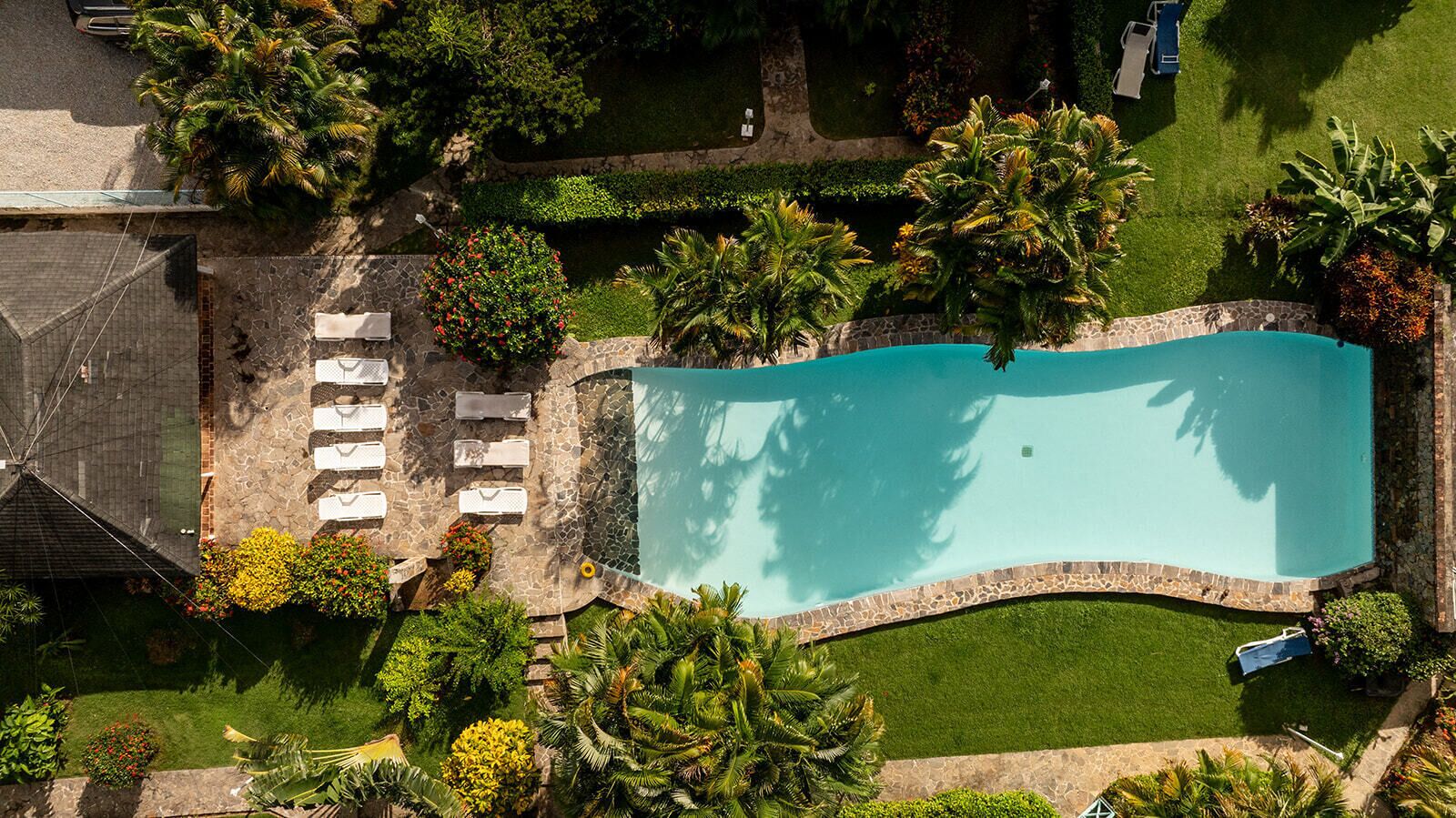 An aerial view of a swimming pool surrounded by a stone wall, with a lawn and palm trees.