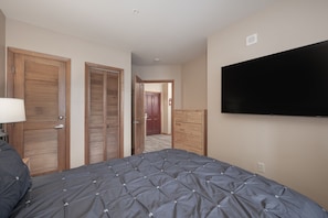 A bedroom with a bed, wooden closets, a television, and a door leading to another room. - NEW! Premium Unit 2216 - 1 Br - Zephyr Mountain Lodge (Winter Park)