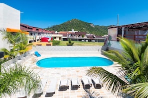 A swimming pool with lounge chairs, surrounded by palm trees and a view of a hillside.