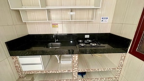 A kitchen with a black countertop, stainless steel sink, and gas stove. There is a small cabinet below the countertop and a tiled backsplash.