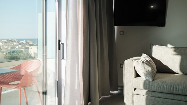 Un salon moderne avec un canapé, un téléviseur et une porte vitrée donnant sur un balcon avec vue sur la ville.